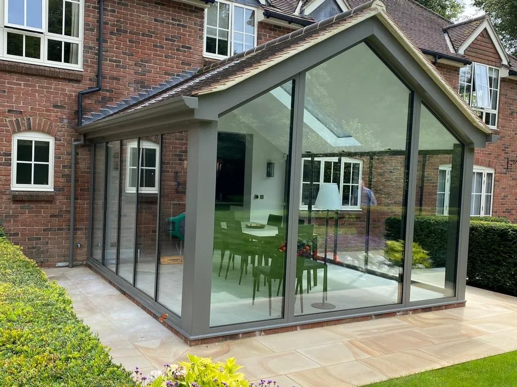 Anthracite bifold doors in a glass sunroom extension with floor to ceiling windows and a dining area inside. The anthracite grey doors open out onto the patio