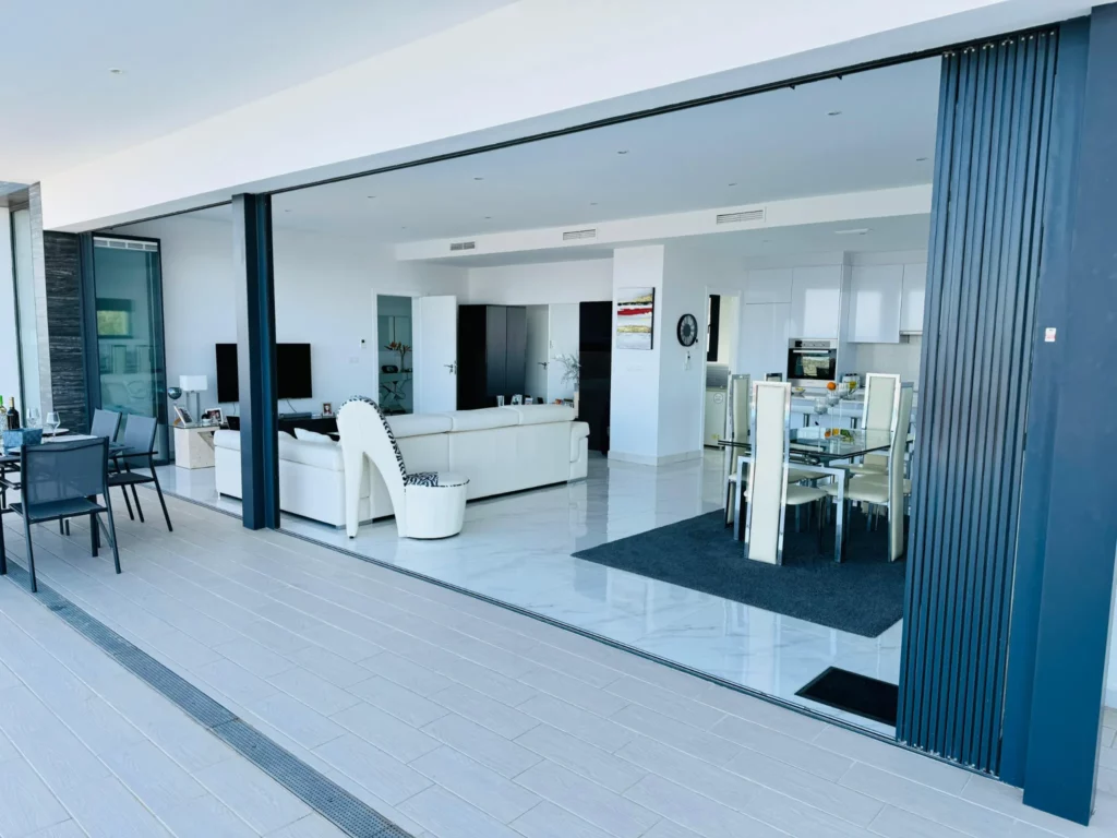 Open plan cool blue living room and kitchen with outside area, separated with large bifold doors